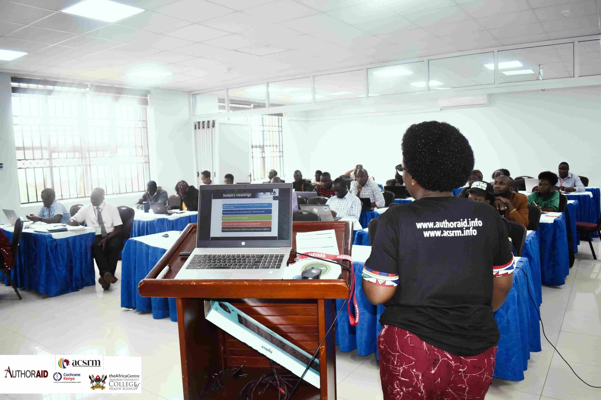 Researchers working on laptops during an SRN systematic review workshop while a facilitator presents at the lectern.